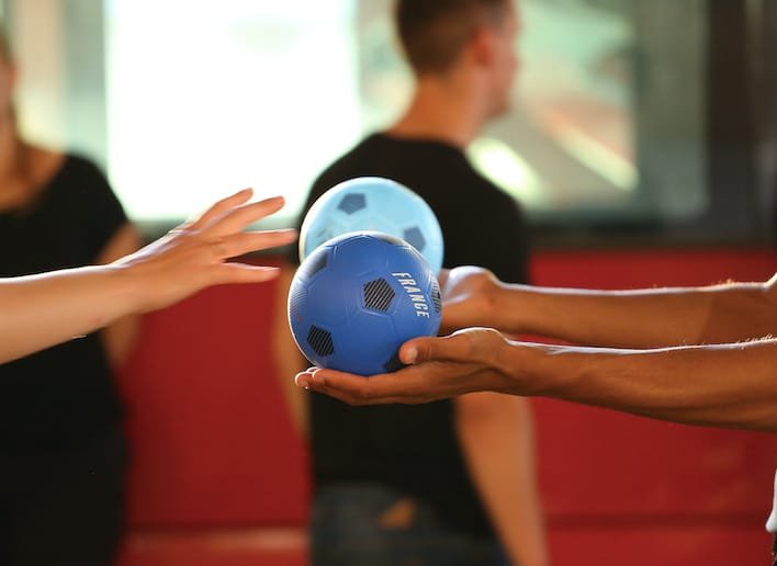 Main d'une personne qui tend un ballon bleu vers la main d'une autre personne