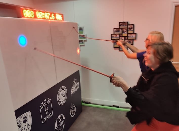 Groupe de deux personnes jouant à l'escrime sur le mur digital avec une épée
